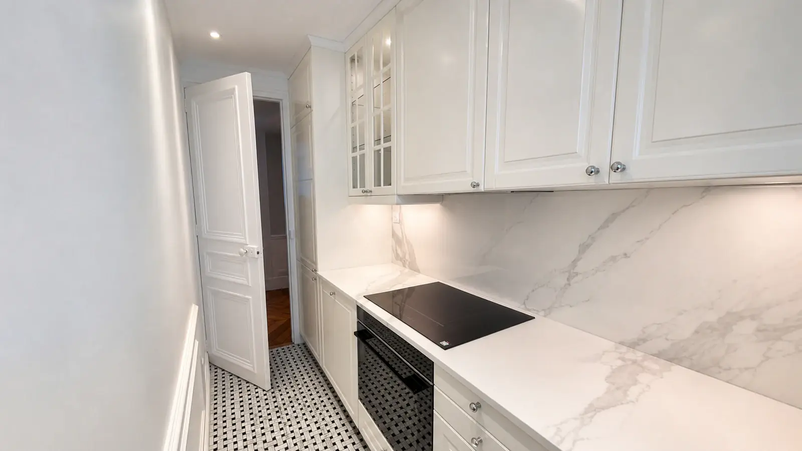 Cuisine étroite rénovée avec façades moulurées blanches, plan de travail effet marbre, plaque à induction et sol en mosaïque